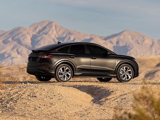 Sedán negro con vinilo decorativo mate estacionado sobre la tierra con montañas al fondo.
