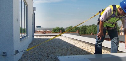 Worker on roof connected to permanently mounted anchor system attached to structure on roof

