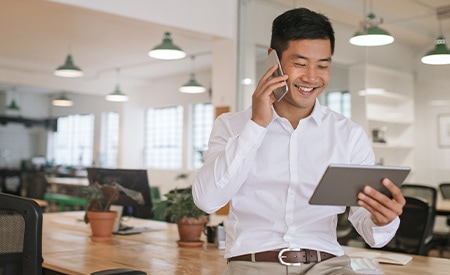 Imagen de un empresario sonriente hablando por teléfono y mirando una tableta.
