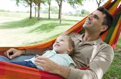 Father and son swing in a hammock and looking at trees.