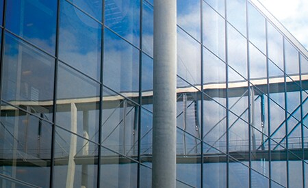 Edificio con grandes ventanales que reflejan el cielo y las nubes.
