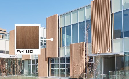 Exterior de un edificio con fachada de cristal y madera, con mención del producto acabado exterior Walnut DINOC.
