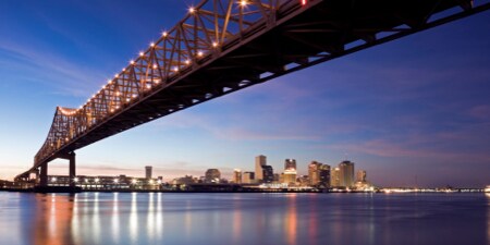 Long bridge illuminated with lights crossing a large expanse of water into a city.
