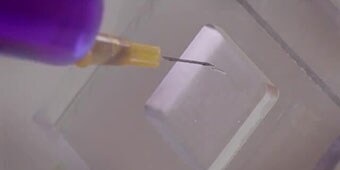 Imagen de video de una aguja insertando líquido teñido entre paneles de plástico adheridos para mostrar resistencia a la intrusión de humedad

