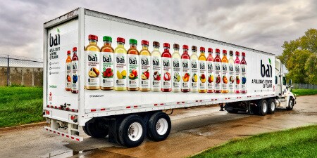 Imagen de una camion ploteado con ilustraciones de botellas de diversas frutas
