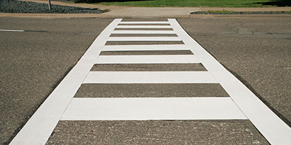 Low-angle shot of white painted crosswalk across road.
