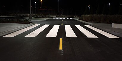Highly visible pavement markings, including crosswalk and lane dividing line, at night.
