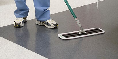 Una persona limpiando el piso de una instalación con un paño.
