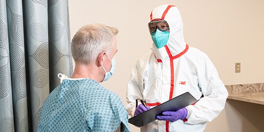 Clinician wearing PPE speaking with a patient
