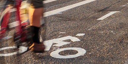 Blurred bicyclist in bike lane with white biker symbol and white arrow on the pavement.
