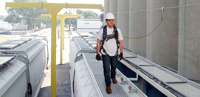 Worker on a railcar connected to a permanent overhead lifeline at a rail loading facility
