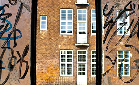 Ventana de tres paneles cuyos paneles laterales tienen grafitis negros que cubren el vidrio, mientras que el panel del medio está limpio y claro con las Películas para Ventanas Anti-Graffiti de 3M.
