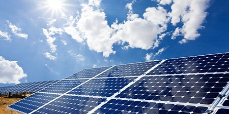 Imagen de paneles solares. Cielo celeste con nubes blancas y rayos de sol.
