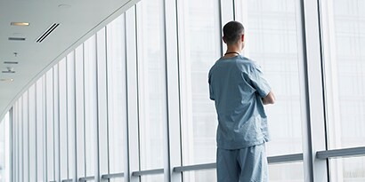 Persona de espaldas mirando hacia afuera a través de una ventana.
