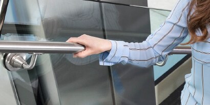 Imagen del brazo de una mujer con camisa celeste y rayas marrones sujetando la baranda metálica de una instalación.