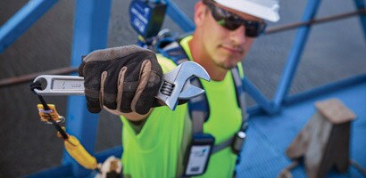 Image of worker holding an adjustable wrench secured to his belt by a tether
