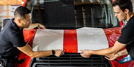 Instaladoes colocando película adhesiva roja y blanca sobre una camioneta.
