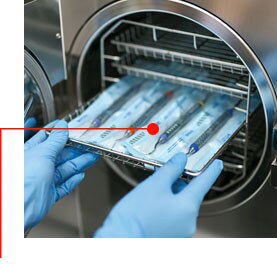 Imagen de manos con guantes quitando una bandeja de instrumentos de un autoclave
